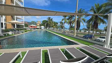 Ein Poolbereich mit Liegestühlen, blauem Himmel und Palmen.