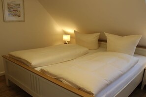 A double bed with white linens and a wooden headboard, a bedside table with a lamp, and a framed picture on the wall. - Holiday home with 2 bedrooms (Krummhörn-Greetsiel)