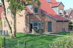 A brick building with a red-tiled roof, a fenced yard, and a table with chairs outside. - Holiday home with 2 bedrooms (Krummhörn-Greetsiel)