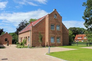 A brick building with a sloped roof, a small annex, and a paved courtyard. - Holiday home with 2 bedrooms (Krummhörn-Greetsiel)