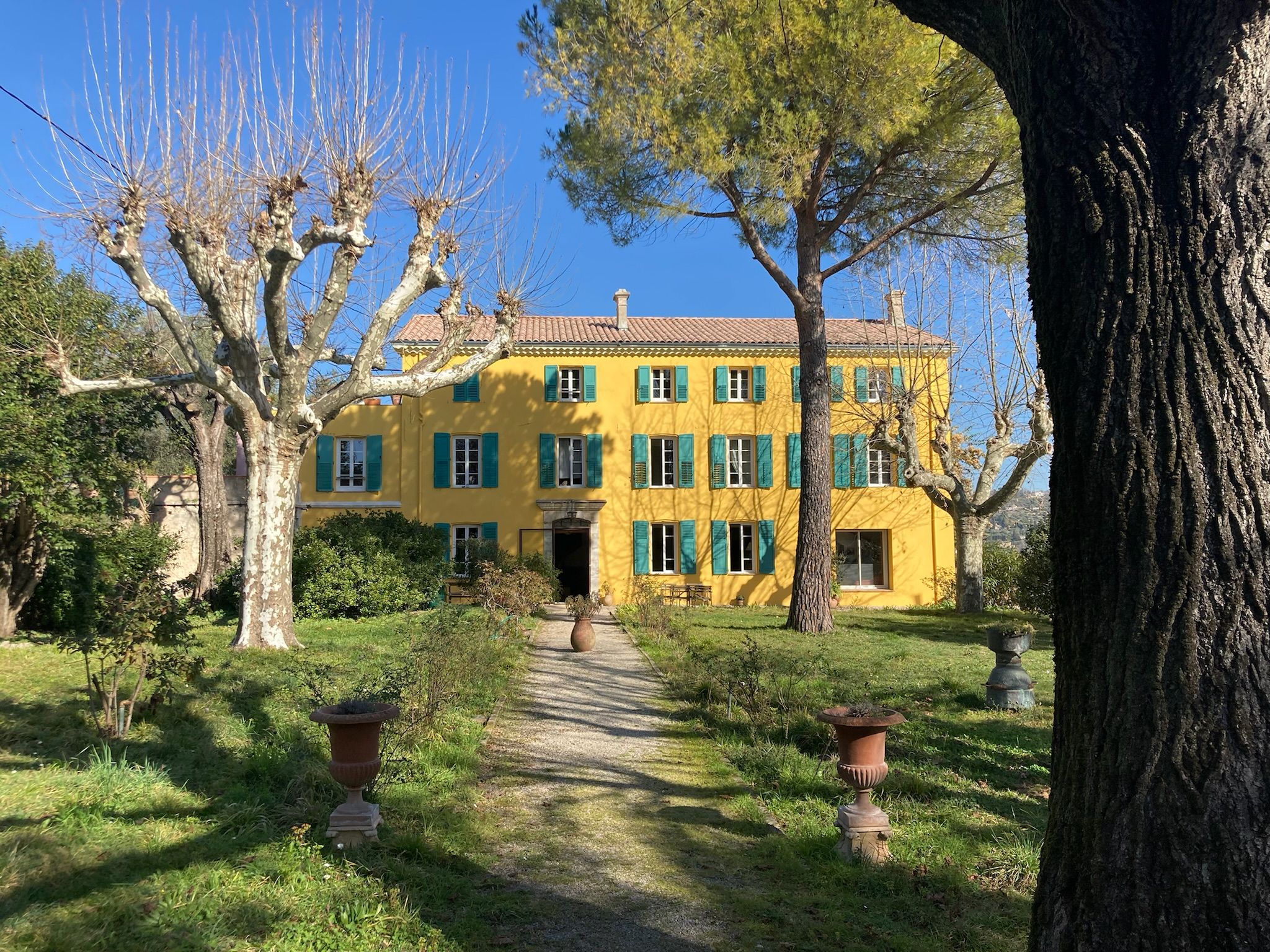 Un bâtiment jaune à la façade symétrique, doté d’une entrée centrale et d’un chemin de gravier menant à cette entrée.
