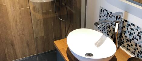 A modern bathroom with a wooden vanity, a white sink, a shower with a glass door, and a tiled backsplash.