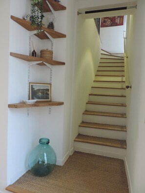 Un escalier avec des marches en bois et une rampe, menant à un palier où est fixée une étagère murale servant à exposer des objets décoratifs.