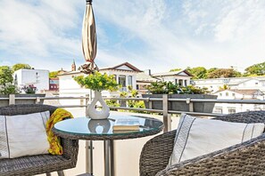 Un balcon agrémenté de meubles en osier, d’une table en verre et d’un vase blanc contenant des fleurs jaunes.