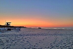 Ein Strand mit Fußabdrücken, einem Rettungsturm und einer Reihe Strandhäuschen.