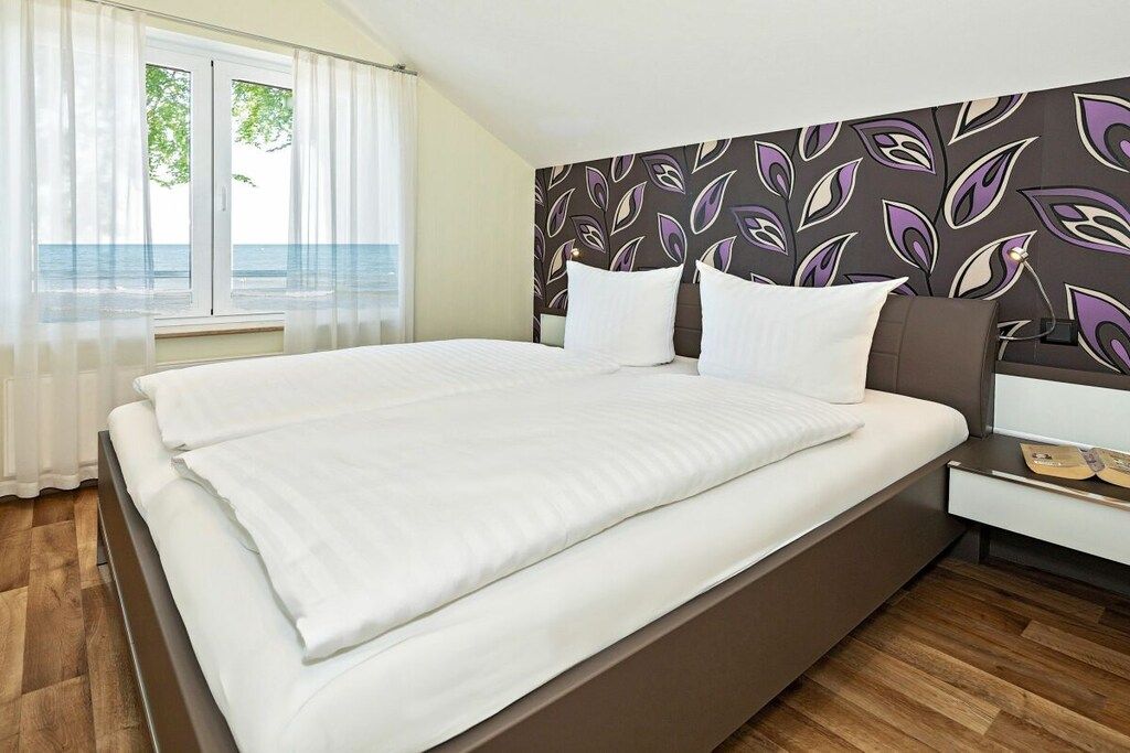 Una habitación de hotel con cama, mesita de noche, ventana con cortinas y una pared con diseño de hojas.