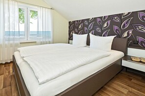 Ein Hotelzimmer mit einem Bett, einem Nachttisch, einem Fenster mit Vorhängen und einer Wand mit einem Blattmuster.