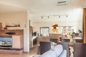 Eine moderne Küche mit Essbereich, ausgestattet mit einem integrierten Fernseher, einem Esstisch mit Stühlen und einer Kücheninsel mit Mikrowelle und Kaffeemaschine.