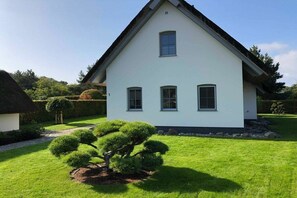 Ein einstöckiges Haus mit weißer Fassade und dunklem Dach, umgeben von einem gepflegten Rasen und einem kleinen Baum.