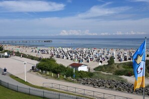 Una playa con un muelle al fondo, una bandera y una fila de carpas.