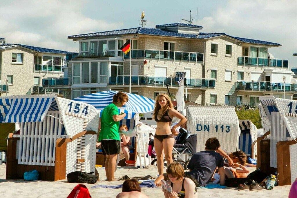 A beach with beach chairs labeled with numbers, a building with balconies, and a flag.