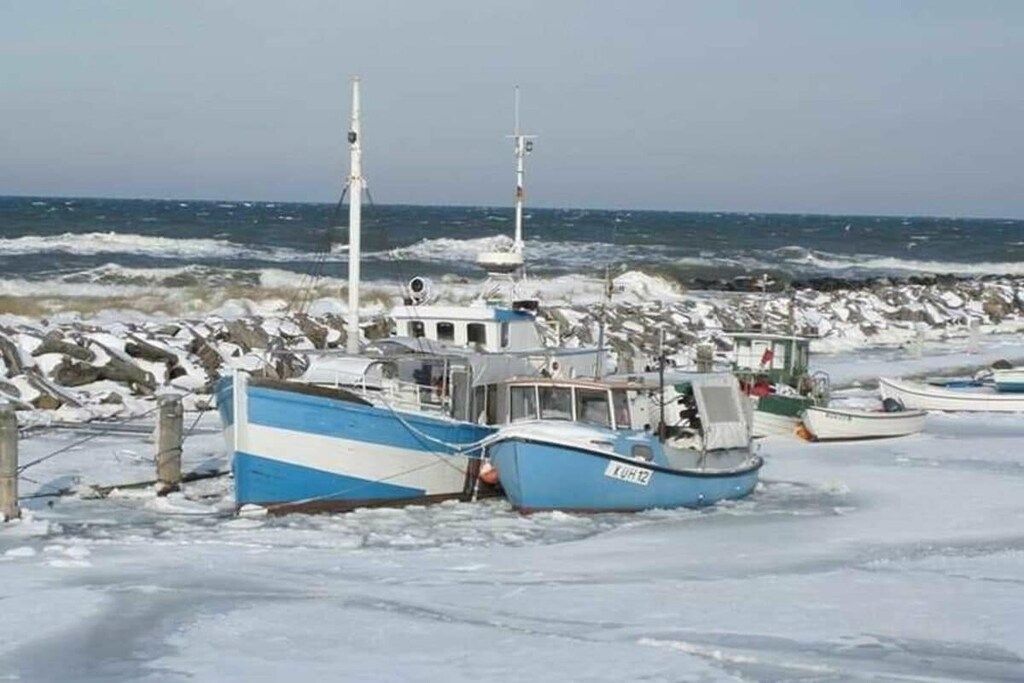 Um barco encalhado no gelo perto de uma costa rochosa.