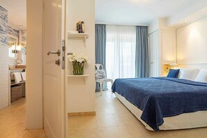 A hotel room with a bed, a bedside table, a chair, a window with curtains, and a bathroom visible through an open door. - Holiday apartment 1 “Kein Hüsung” (Kühlungsborn)