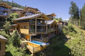 A multi-story wooden chalet with balconies, a hot tub, and a mountainous backdrop. - Premium Chalet #13 with Sauna & Swim Spa (Pichl bei Schladming)