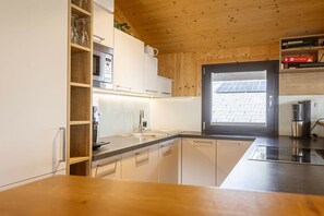 A modern kitchen with a wooden ceiling, built-in appliances, and a window with a view of the outside. - Premium Chalet #13 with Sauna & Swim Spa (Pichl bei Schladming)