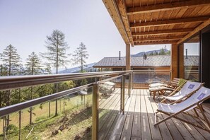 Eine Holzterrasse mit Glastrennwand, die auf eine gebirgige Landschaft blickt.