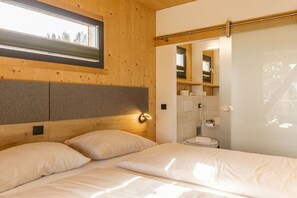A bedroom with a wooden headboard, a window, and a bathroom visible through an open door. - Premium Chalet #13 with Sauna & Swim Spa (Pichl bei Schladming)