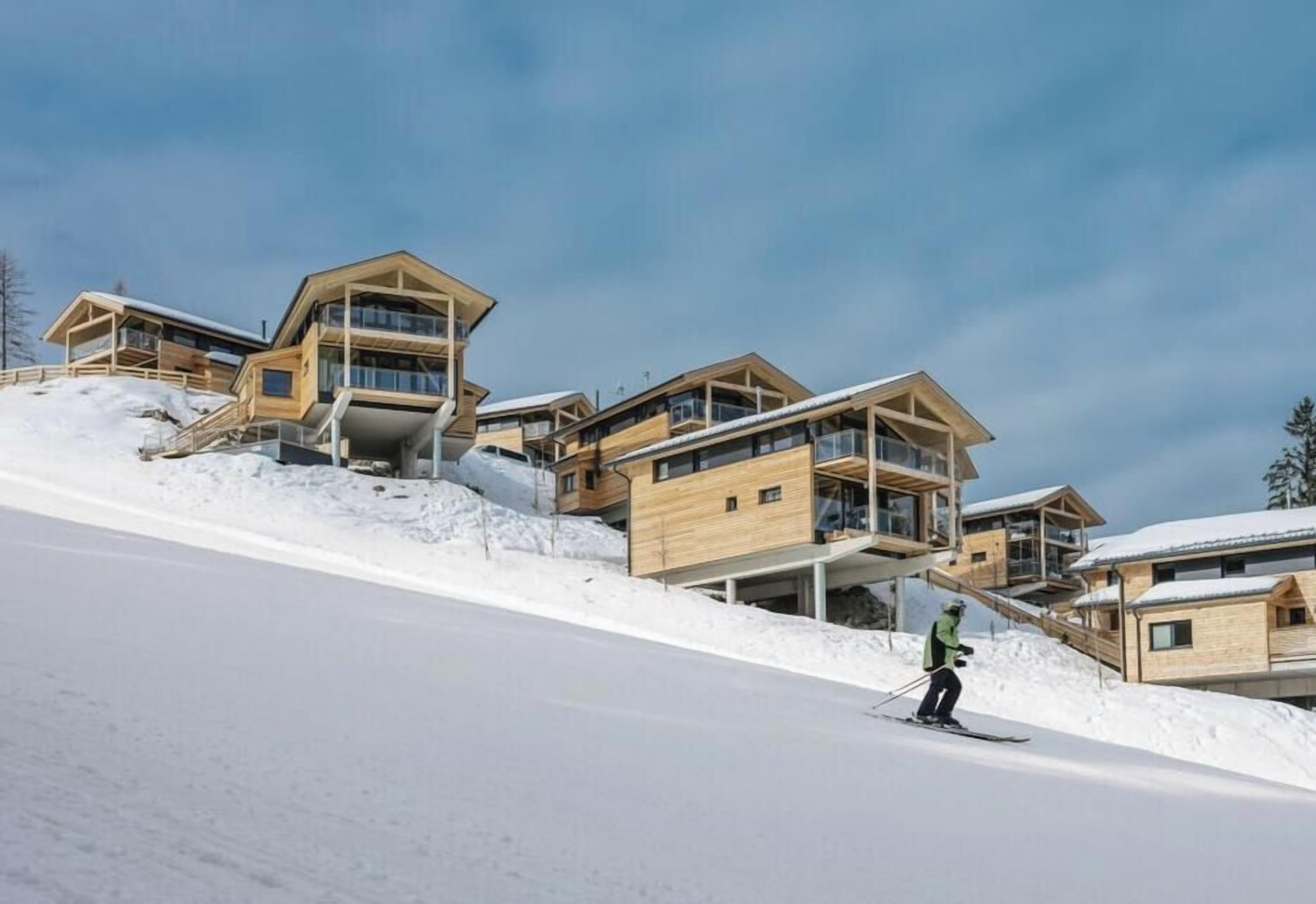 A ski resort with wooden cabins and a skier on a slope.