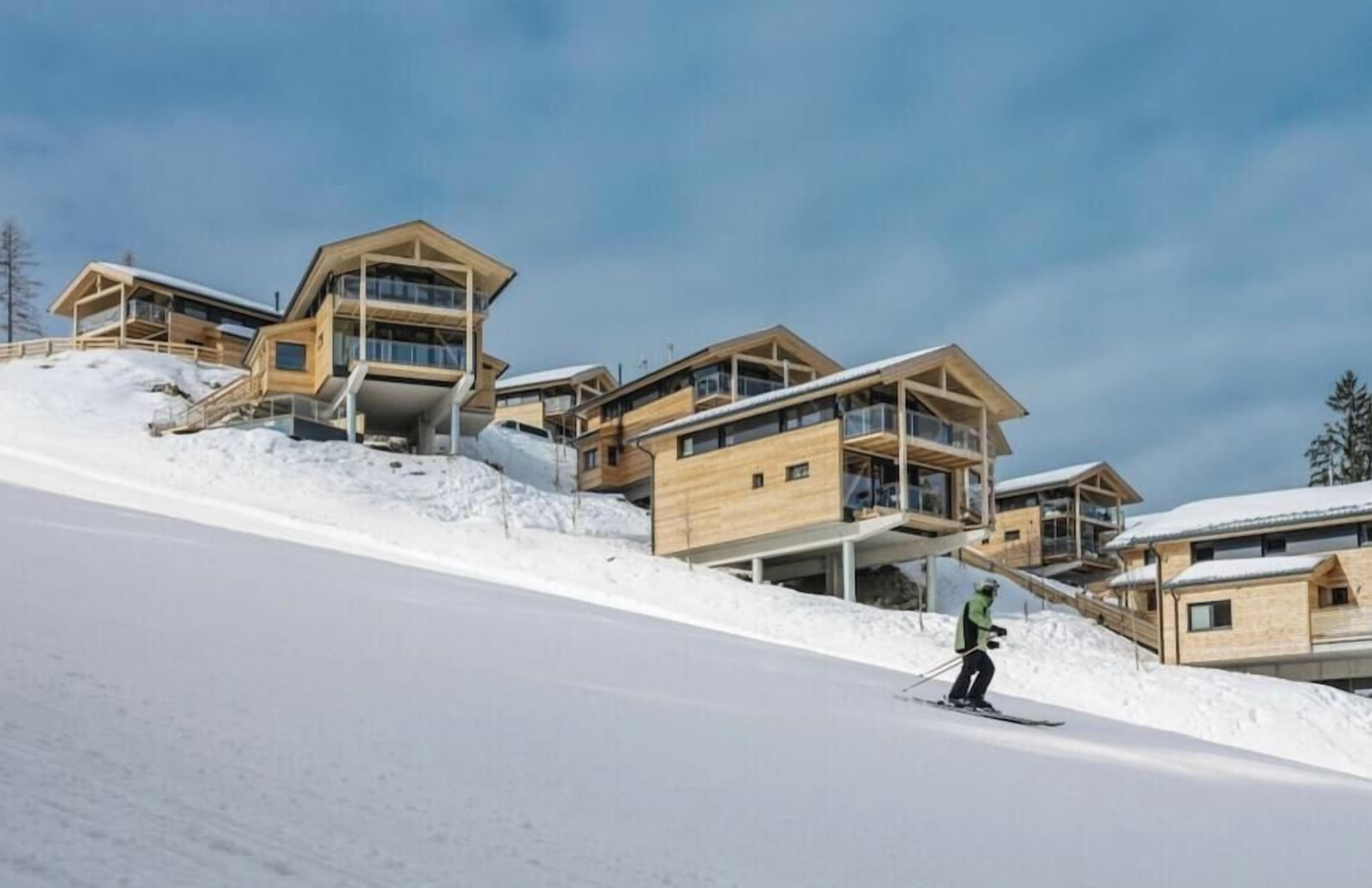 Ein Skigebiet mit mehreren Holzhütten, einer Skipiste und einem Skifahrer.