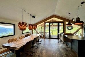 A spacious dining area with a long wooden table and chairs, large windows, and a view of the outdoors. - Cabin in Pichl near Schladming with sauna (Pichl bei Schladming)