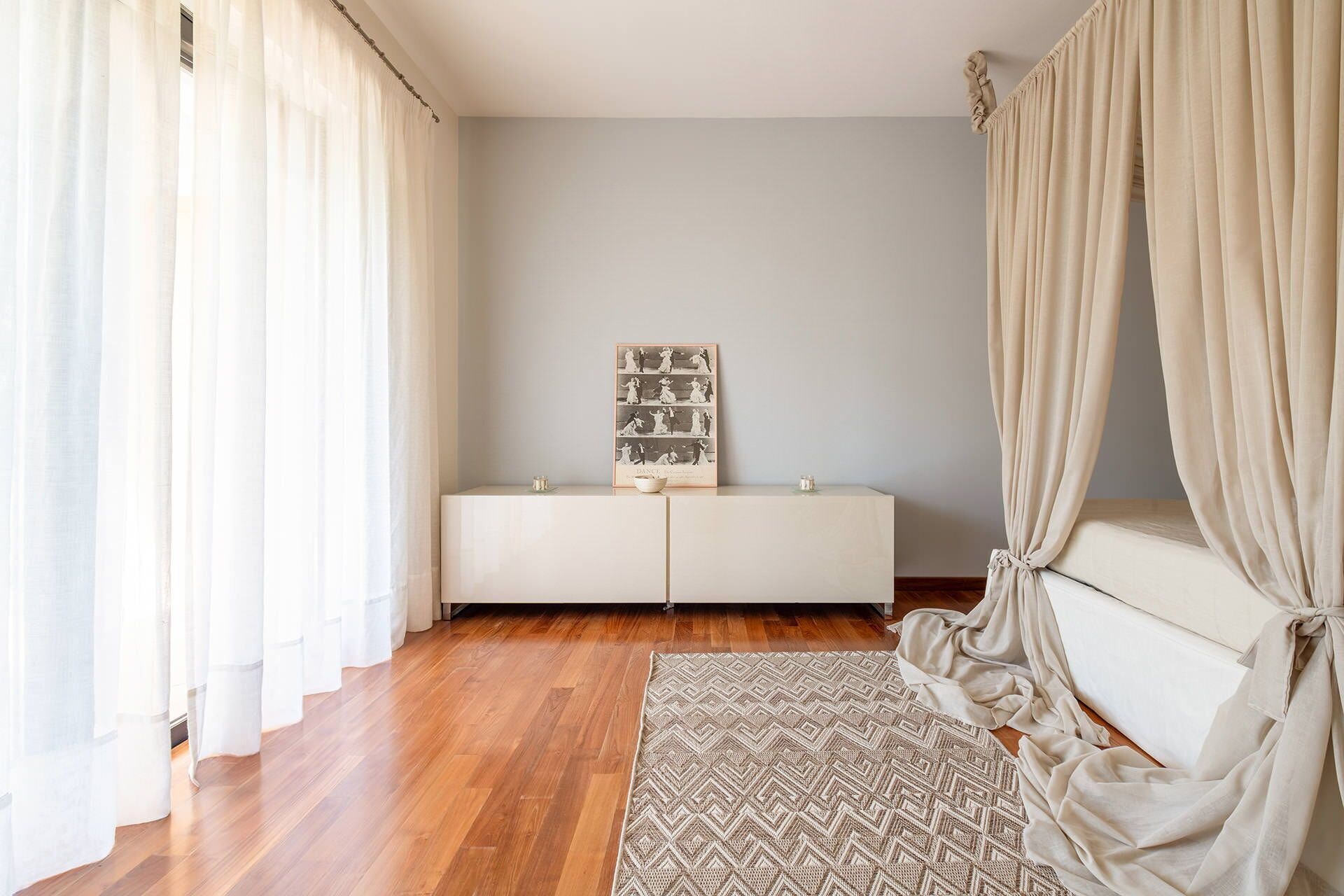 Ein Zimmer mit Holzboden, einer weißen Bank, einem gerahmten Bild und leichten Vorhängen.