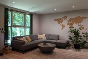 Een moderne woonkamer met een hoekbank, een ronde salontafel en een wereldkaart muurschildering.