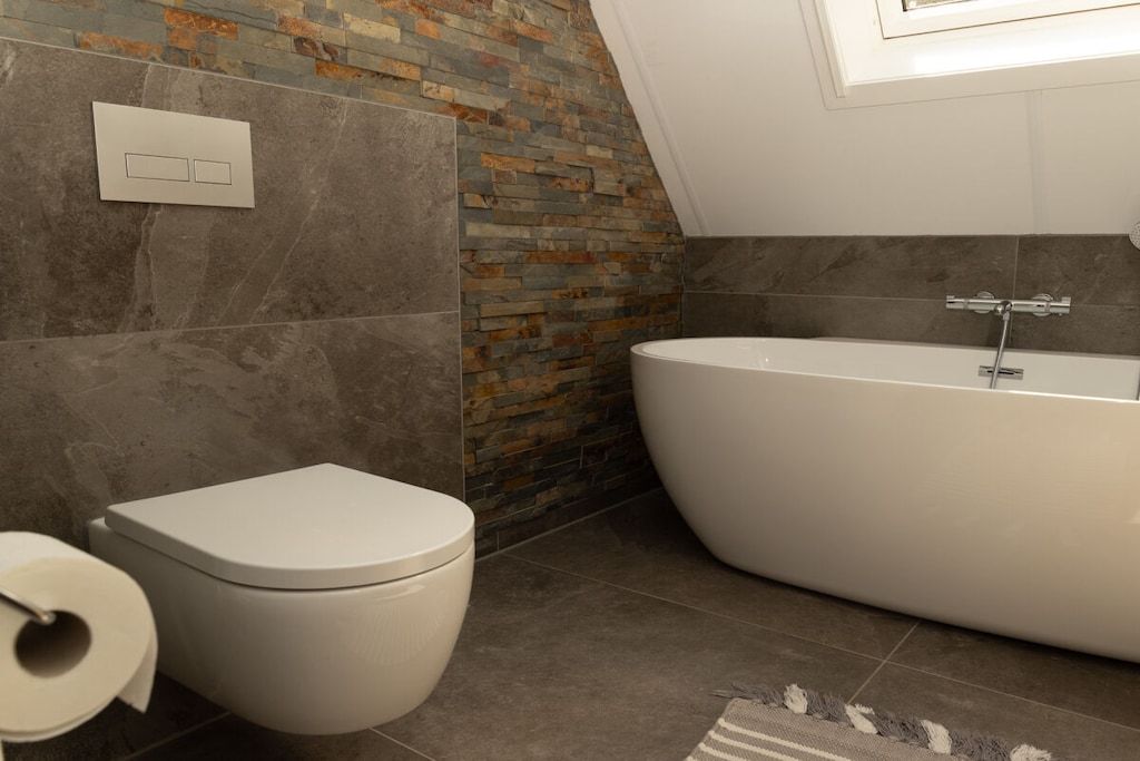 A bathroom with a toilet, a bathtub, and a stone wall.