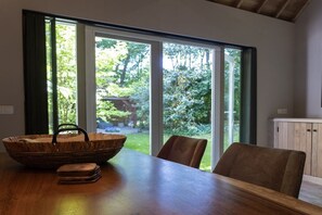A dining area with a wooden table, chairs, a basket, and a view through a glass door to an outdoor garden. - Holiday home with 2 bedrooms (Groot-Valkenisse)