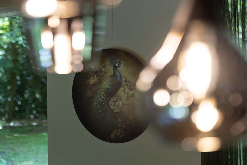 Ein rundes Kunstwerk mit einem Pfau, das an einer Wand hängt.