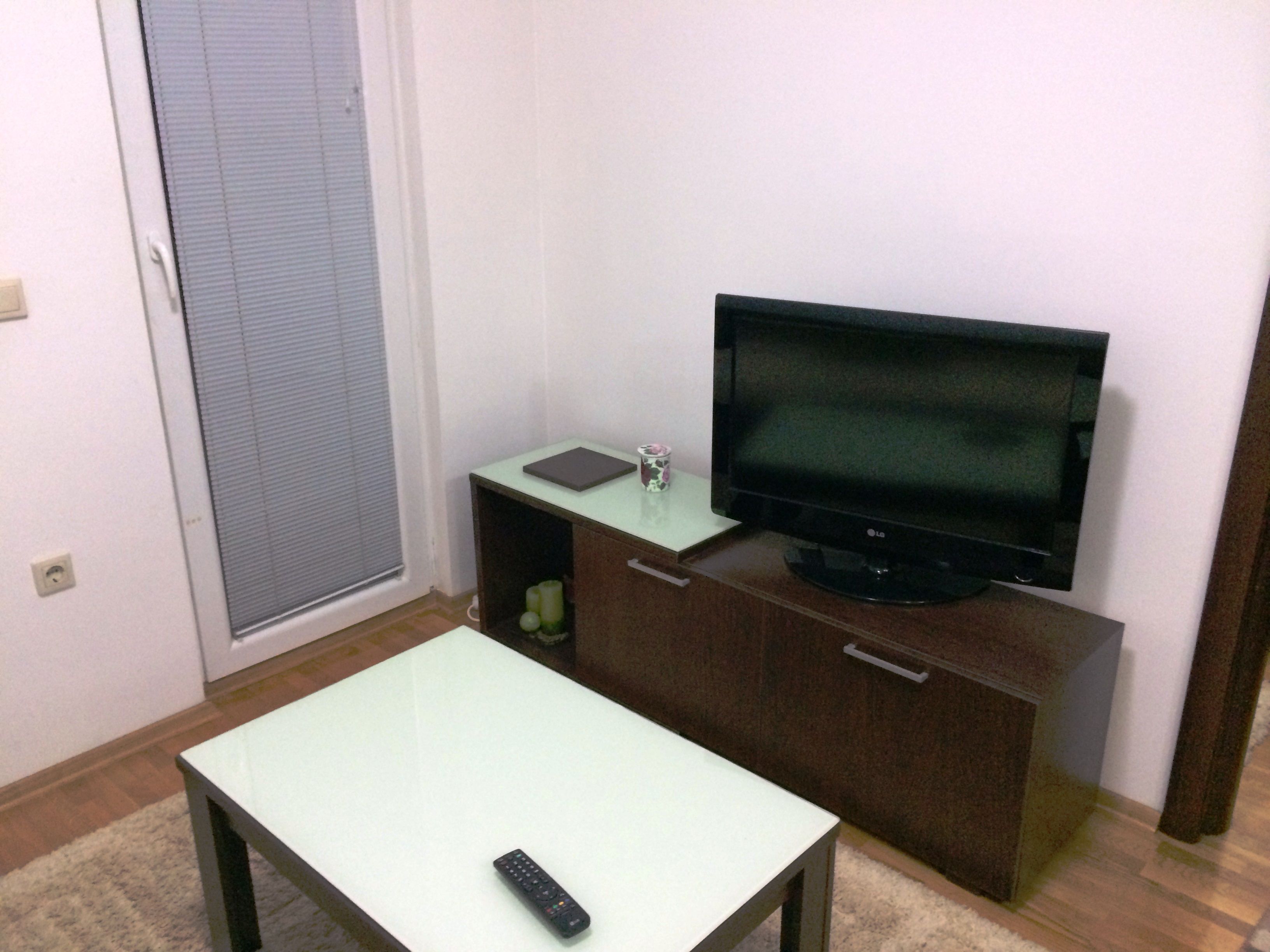 Ein kleines Zimmer mit einem Fernseher auf einem Schrank, einem Tisch und einer Fernbedienung auf dem Tisch.