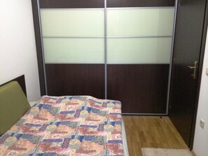 Un dormitorio con cama, piso de madera, armario con paneles de vidrio esmerilado y una puerta.
