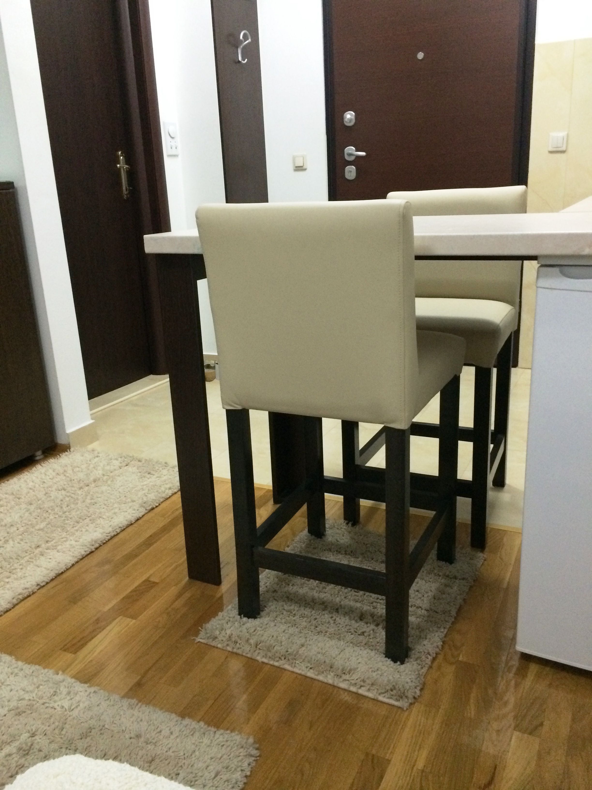 A dining area with a table and chairs, wooden flooring, and a white rug.