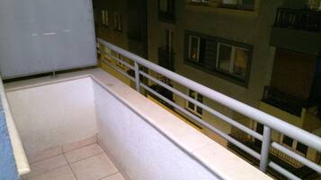 Un balcón con barandilla blanca, suelo de baldosas y vistas a un edificio con varias ventanas y balcones.