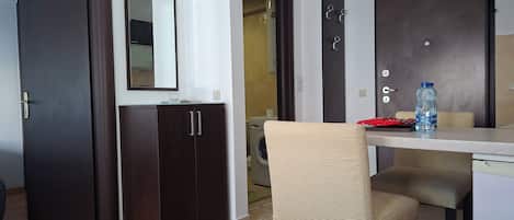 A room with a wooden floor, a dark-colored wardrobe, a mirror, a chair, a table, and a water bottle.