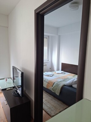 Un dormitorio con una cama, una mesita de noche con televisor y una ventana con persianas.