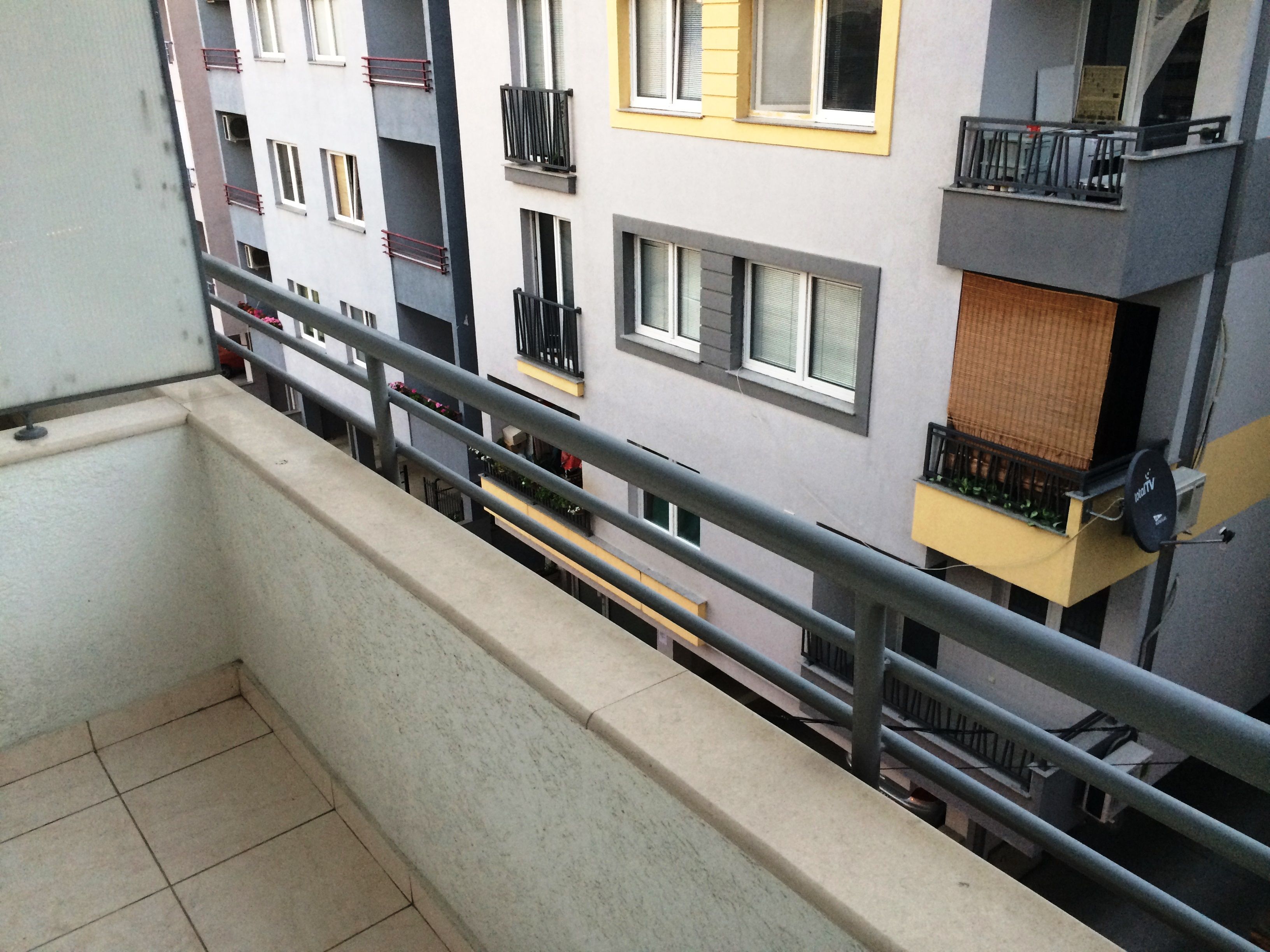 Ein Balkon mit Metallgeländer, der auf ein mehrgeschossiges Wohngebäude mit Balkonen und Fenstern blickt.