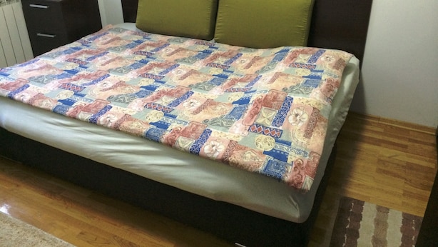 Un letto con una coperta a motivi, un poggiatesta verde e un comodino con un recipiente in vetro.