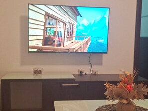 A television mounted on a wall, a small table with a glass container, and a decorative plant arrangement. - Fortuna Fortis Apartments - Suite 7 (Skopje)