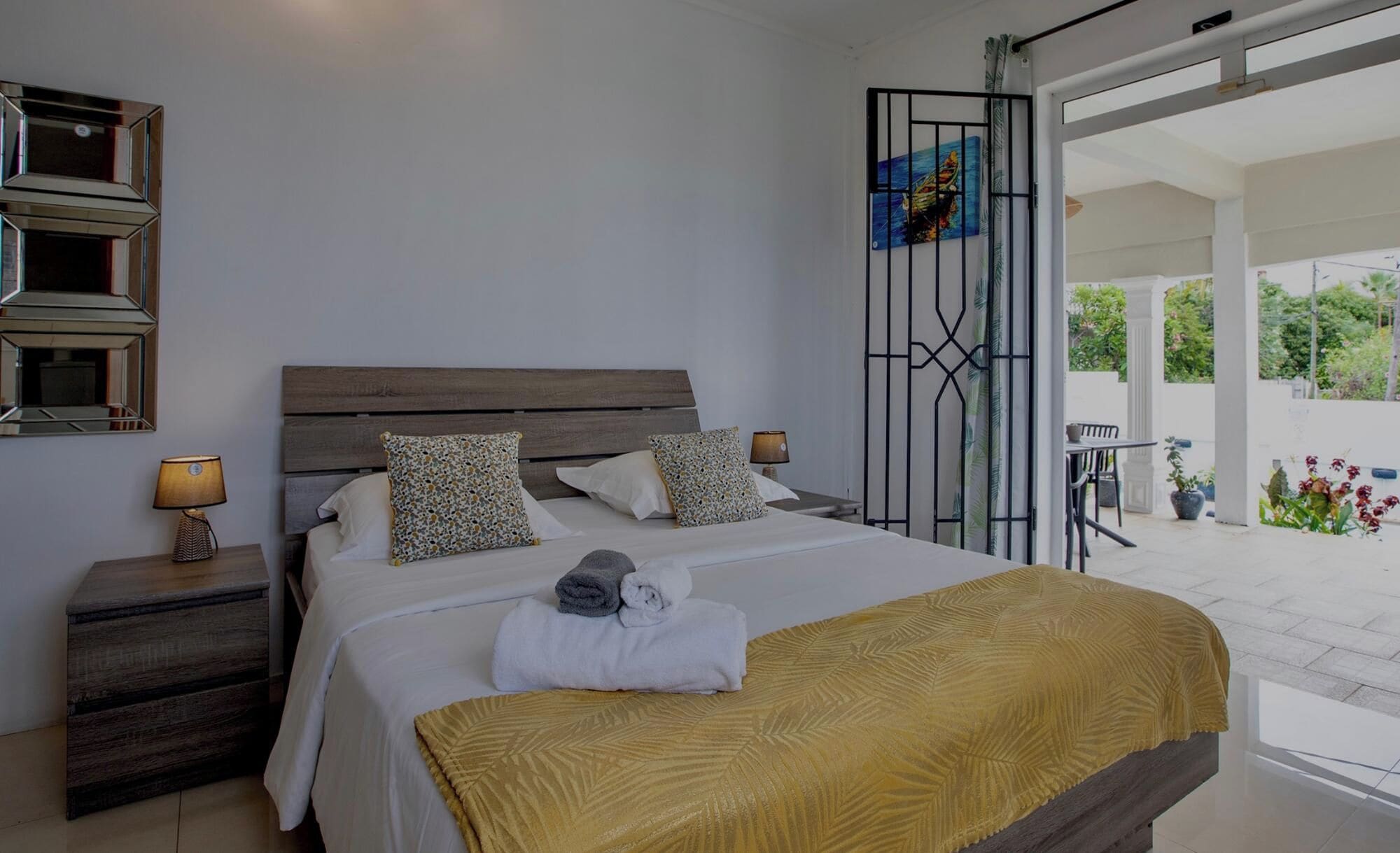 Une chambre à coucher avec un lit, des oreillers, une table de chevet, une lampe et une vue sur l’extérieur.