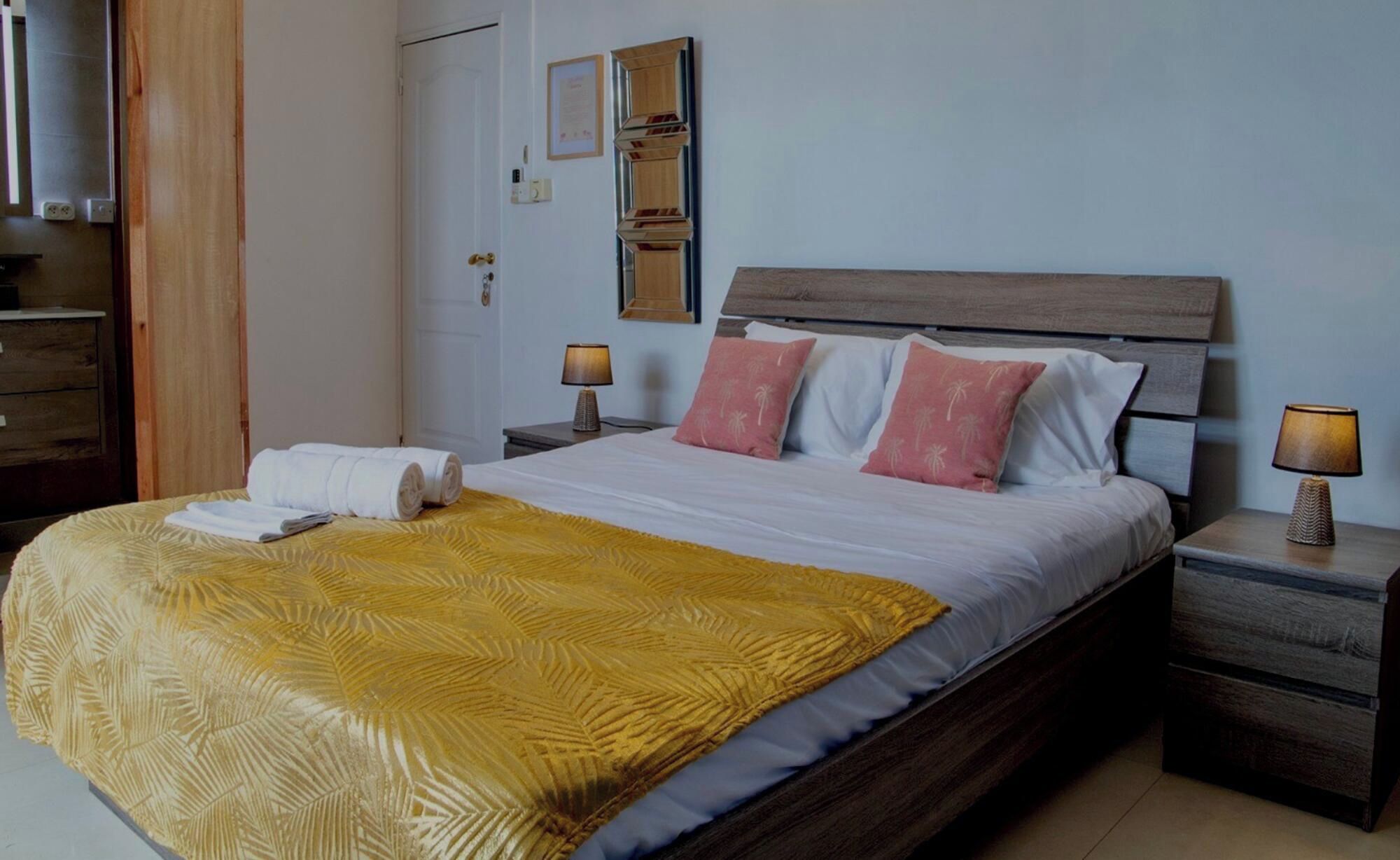 A hotel room with a bed, two bedside tables, a wooden headboard, and a wall-mounted mirror.