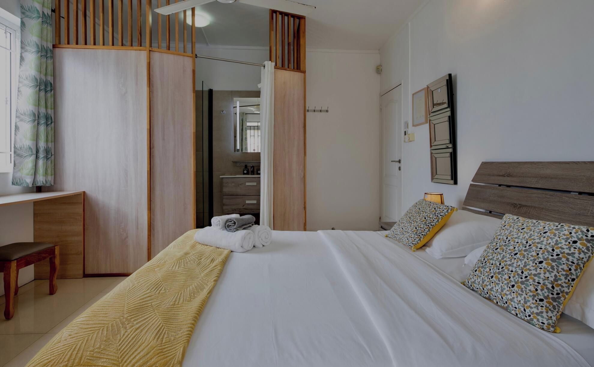 A hotel room with a bed, a desk, a bench, and a bathroom visible through a sliding door.
