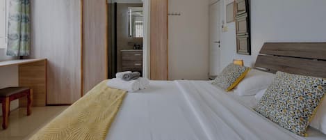 A hotel room with a bed, a desk, a bench, and a bathroom visible through a sliding door.