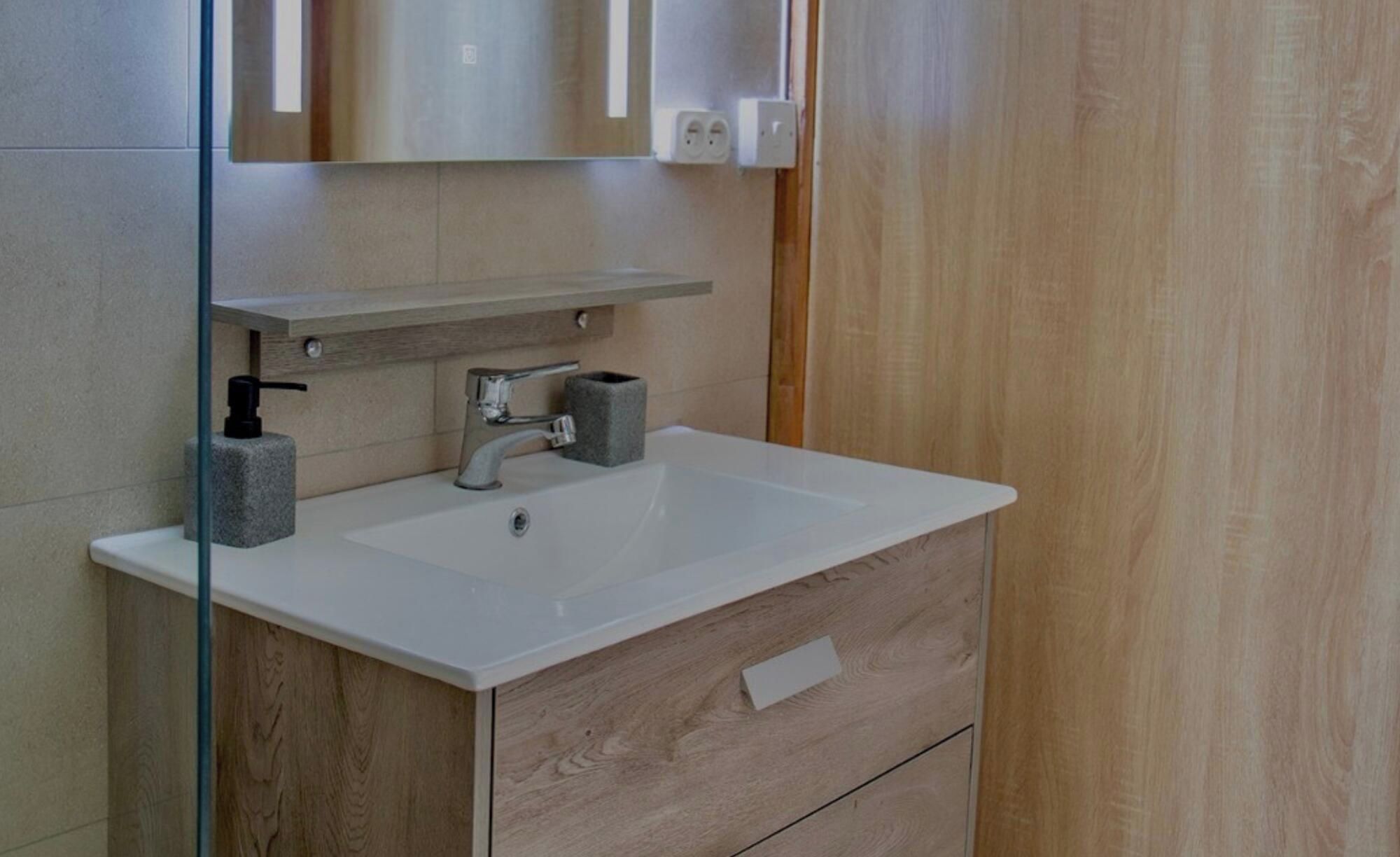 Une salle de bain avec un lavabo blanc, un miroir et un meuble-lavabo en bois.