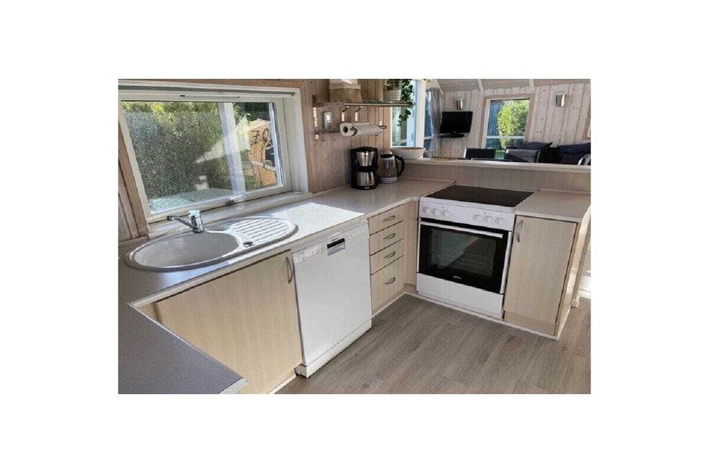 A compact kitchen with a sink, dishwasher, stove, and a window providing natural light.