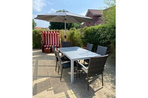 Een terras buiten met een tafel, stoelen en een parasol.