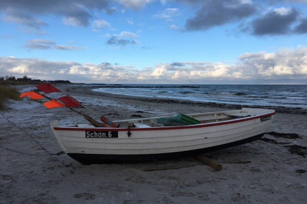 A small boat named 'Schön.6' on a sandy beach with the sea in the background.
