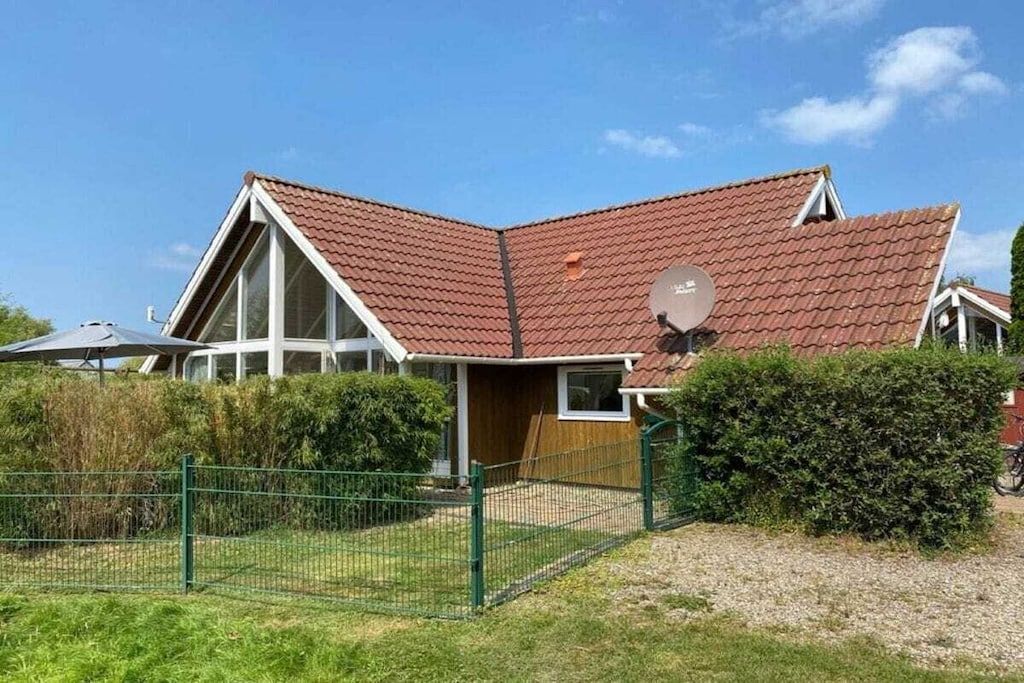 Une maison avec un toit en pente, une antenne parabolique et une cour clôturée.