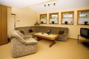 Ein Wohnzimmer mit Sofa, Sessel, Couchtisch und Fernseher.