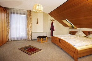 Ein Schlafzimmer mit schrägen Wänden, einem Bett, einem Heizkörper, einem Fenster mit Vorhängen und einer Hängelampe.
