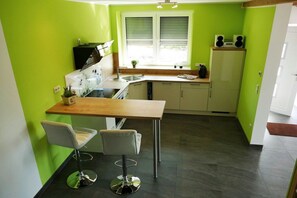A compact kitchen with a wooden countertop, two bar stools, a built-in oven, and a window with blinds.